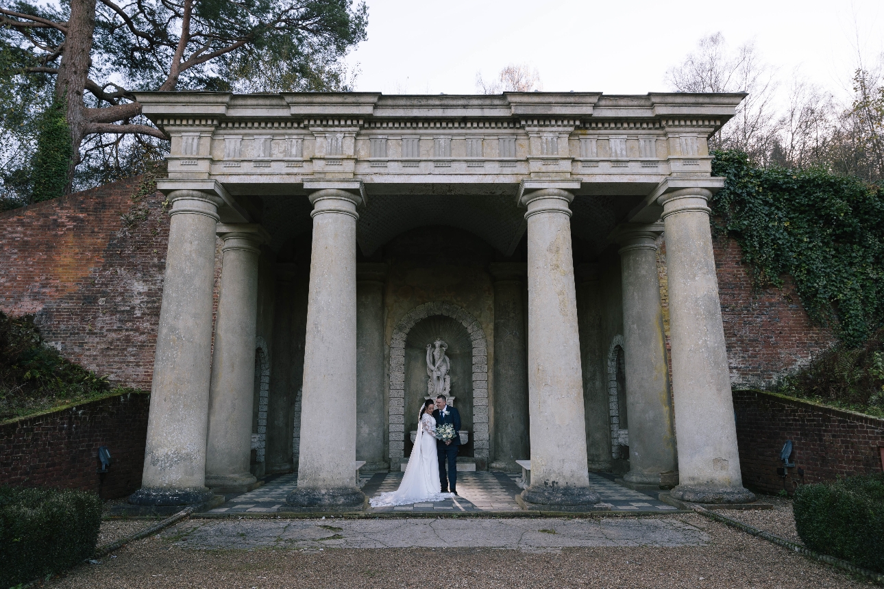 bride and groom standing outside under stone pillars