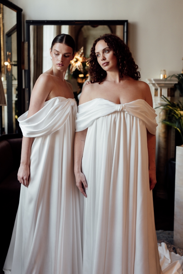 two models in drapped wedding dresses in white off shoulder 